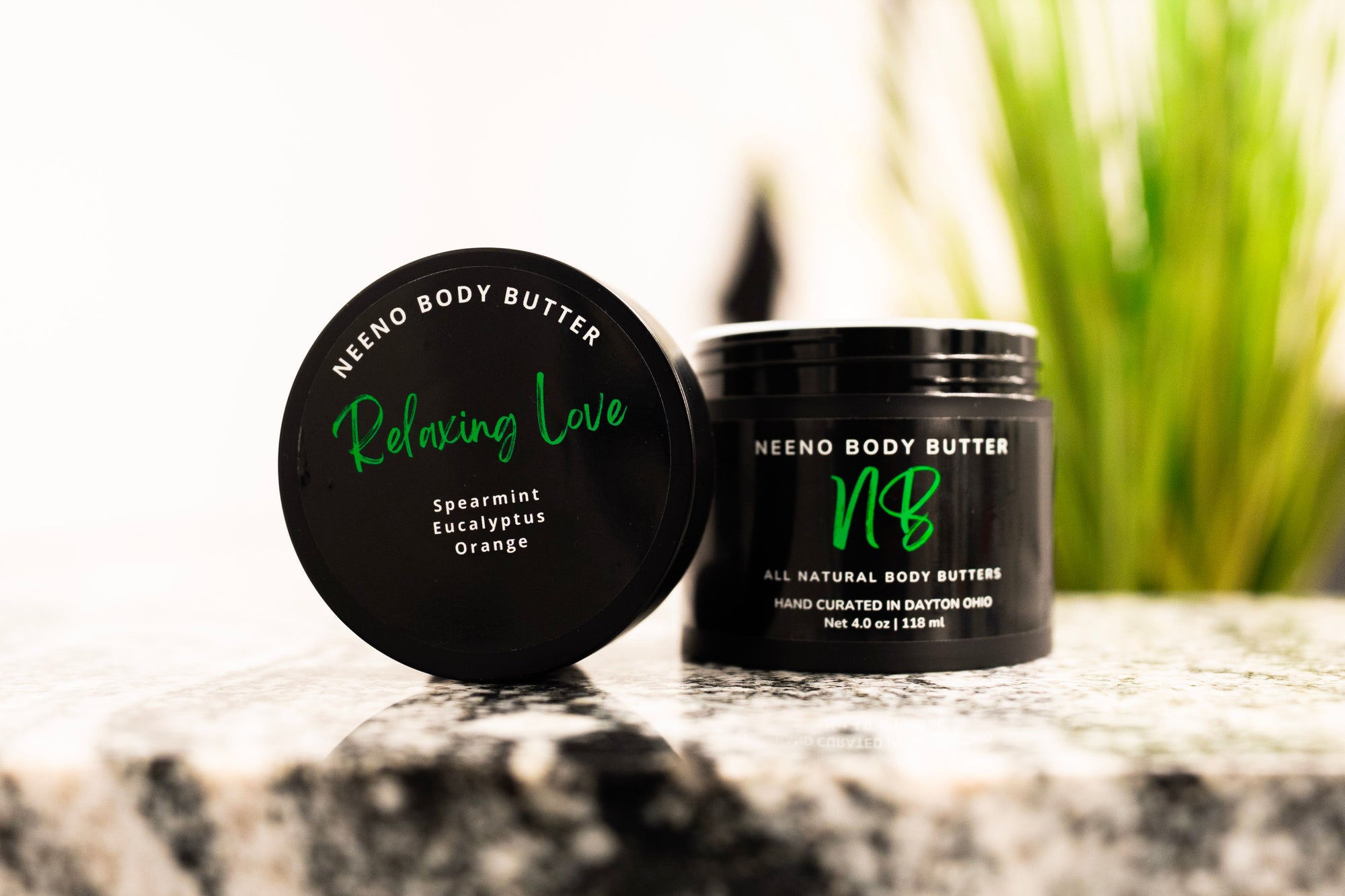 Relaxing Love whipped body butter in a Neeno Body black jar on a marble countertop, green plant in the back